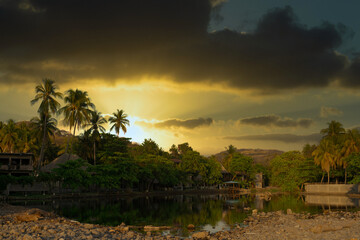 Obraz premium Sunset over touristic village in El Tunco, El Salvador with overcast. Huts covered by palm trees on the shore of Rio Grande river