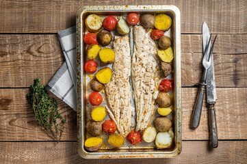 Hake fish fillet, roasted fish meat with tomato and potato. Wooden background. Top view
