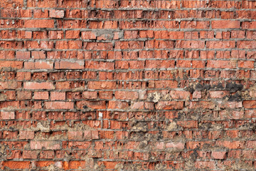 View of an old cracked wall of red, gray and brown brick and mortar.