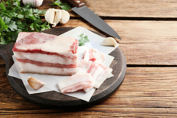 Tasty salt pork with garlic and parsley on wooden table, space for text