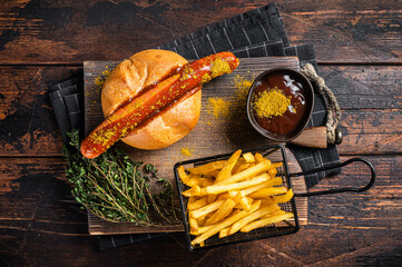 Currywurst Bratwurst sausage in a bun with curry sauce and French fries. Wooden background. Top view