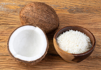 Grated coconut flakes in a bowl with fruit over wooden table
