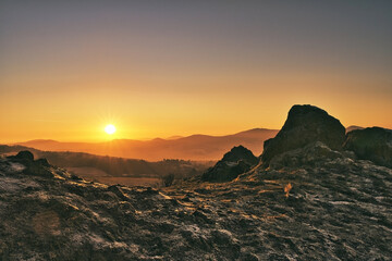 Sun peaking over the mountains in germany beside a large rock formation