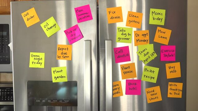 Refrigerator Door Filled With Reminder Notes and Hand Adds Taxes Due April 18th Memo Over File Taxes Memo