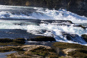 Famous Rhine Falls with rocks, spray and splashing water on a sunny spring day. Photo taken March 5th, 2022, Zurich, Switzerland.