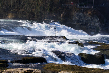 Famous Rhine Falls with rocks, spray and splashing water on a sunny spring day. Photo taken March 5th, 2022, Zurich, Switzerland.