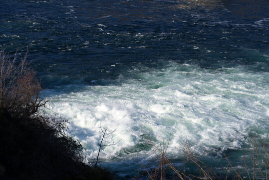 Famous Rhine Falls with rocks, spray and splashing water on a sunny spring day. Photo taken March 5th, 2022, Zurich, Switzerland.