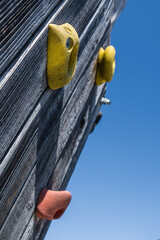 Detail einer Kletterwand aus Holz mit bunten Klettergriffen und blauem Himmel