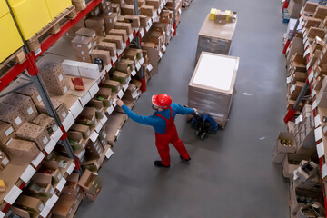Obraz premium Man in hardhat working with pallet truck at warehouse, above view. Logistics center