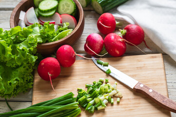 Fresh spring salad of radishes, cucumbers and herbs. Mode green onions on a wooden board.