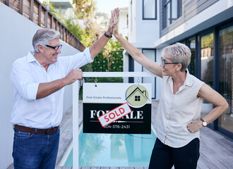 Another happy customer. Cropped shot of two mature people high fiving while standing in front of a for sale board with a sold sticker on it.