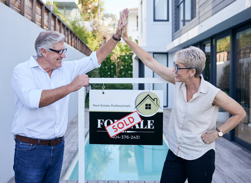 Another Happy Customer. Cropped Shot Of Two Mature People High Fiving While Standing In Front Of A For Sale Board With A Sold Sticker On It.