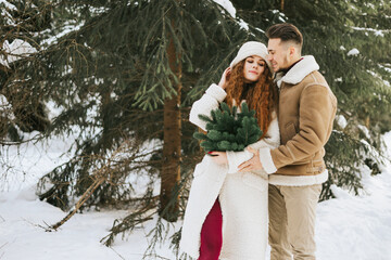 young couple in love man and woman in fashion stylish winter clothes standing in snowy pine forest and having fun spending time together, concept of valentine's day and newlyweds, tenderness and love