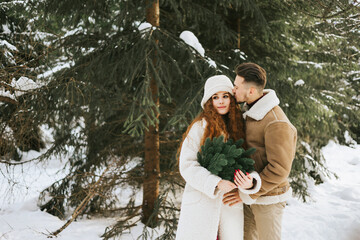 young couple in love man and woman in fashion stylish winter clothes standing in snowy pine forest and having fun spending time together, concept of valentine's day and newlyweds, tenderness and love