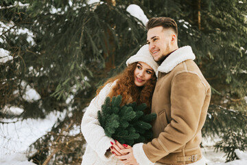 Obraz premium young couple in love man and woman in fashion stylish winter clothes standing in snowy pine forest and having fun spending time together, concept of valentine's day and newlyweds, tenderness and love