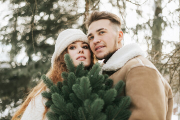 Fototapeta premium young couple in love man and woman in fashion stylish winter clothes standing in snowy pine forest and having fun spending time together, concept of valentine's day and newlyweds, tenderness and love