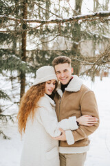 young couple in love man and woman in fashion stylish winter clothes standing in snowy pine forest and having fun spending time together, concept of valentine's day and newlyweds, tenderness and love