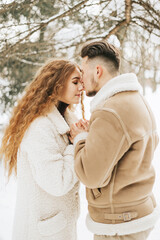 Fototapeta premium young couple in love man and woman in fashion stylish winter clothes standing in snowy pine forest and having fun spending time together, concept of valentine's day and newlyweds, tenderness and love