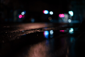 Closeup of a wet asphalt road reflecting bokeh blurry lights at night