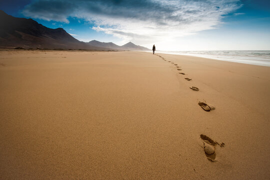 Person walking on sandy shore surrounded by hills