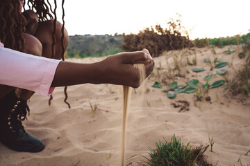 Crop black woman with handful of sand on seashore