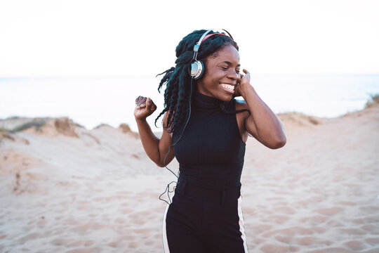 Carefree black woman listening to music on beach