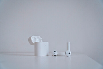 Wireless earphones and the open charging case on a white table against a white wall