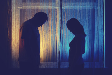 Silhouette of sad man and woman in a quarrel against the background of a night window. Divorce of...
