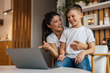 Young son using a laptop with his mother, smiling faces.