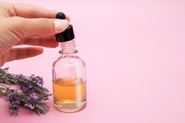 Womans hand draws liquid into a pipette from a glass bottle on a pink background with lavender...