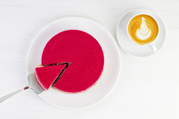 Homemade raspberry and strawberry cheesecake and cup of coffee cappuccino on white wooden table. Top view.