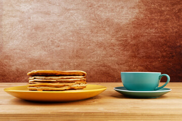 Stack of homemade pancakes in a yellow plate and cup of coffee or tea on wooden table. Copyspace.