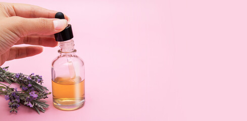 Womans hand draws liquid into a pipette from a glass bottle on a pink background with lavender...