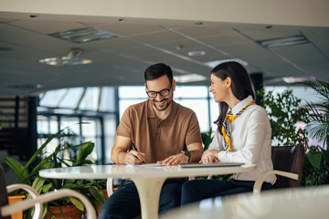 Cheerful caucasian man, signing a job contract with his female assistant.