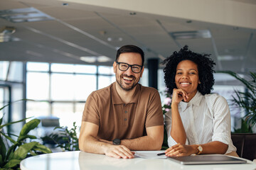 Portrait of a male and female, in the meeting room, smiling at the camera.