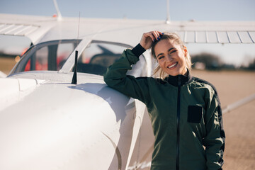 Portrait of cheerful caucasian female aviator, smiling for the camera, near the plane.