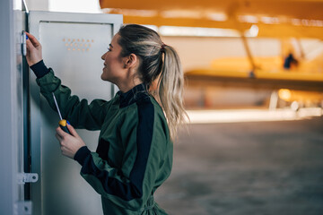Hardworking female plane mechanic, holding a screwdriver, checking her locker.