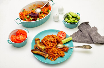 Jollof rice with fried banana on a plate. Rice with tomatoes, onions, spices. Fresh vegetables. White background.