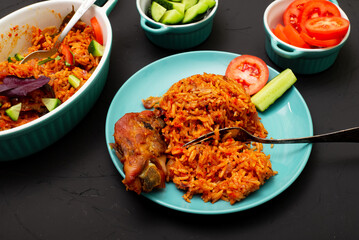 Jollof rice with chicken meat on a plate. Rice with tomatoes, onions, spices. Traditional national Nigerian food. Dark background.