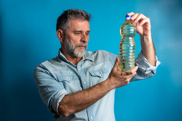 senior grey haired man in front of blue background looking at bottle of oil