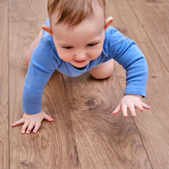 Happy baby toddler crawls on a wooden laminate. Funny child on the parquet in the home living room,...
