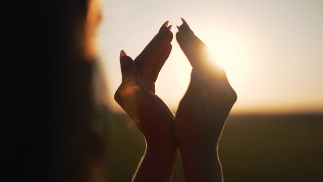 Happy girl in park at sunset. Figure made by fingers. Hands of girl shape of heart. Summer dream. Happiness of freedom in field at sunset. Sunlight between fingers. Silhouette of happy girl in park