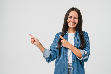 Confident happy young caucasian woman in denim shirt looking at camera pointing at copy space...