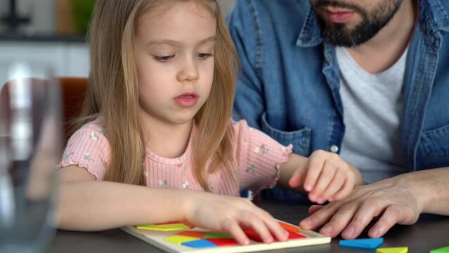 Little child puts colored tangram puzzle with father. Happy girl spends leisure time collect wooden jigsaw. Education concept.