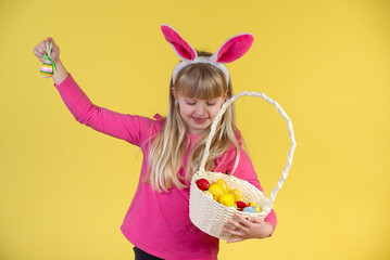 Cute little girl is holding a basket with Easter eggs. Yellow studio background