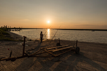 Pêcheur au bord d'une anse maritime au coucher du soleil, à contre-jour, sur une cale de mise à...