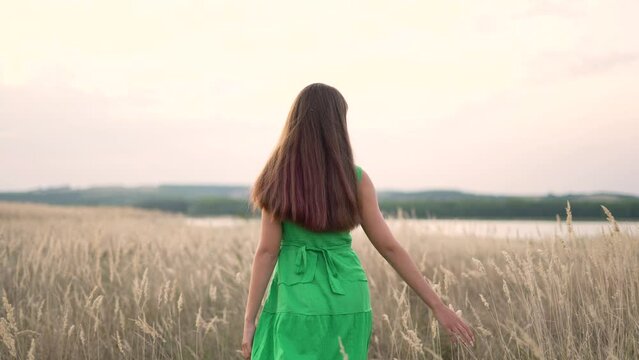 Young girl outdoors in park. Man walks on the grass in the field. Girl alone in nature. Teenager in the park walk on the grass. Girl in a green dress in the field. Teenager summer walk in natural park