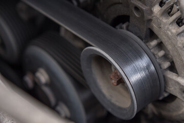 Close-up of the drive belt and the alternator roller in the car engine. Dirty motor.