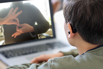 Deaf teenager boy Wearing Hearing Aid using Laptop. Disable student with disabilities deafness distancing learning online from home making communication hands language with teacher via VDO call.