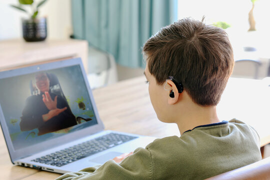 Deaf teenager boy Wearing Hearing Aid using Laptop. Disable student with disabilities deafness distancing learning online from home making communication hands language with teacher via VDO call.